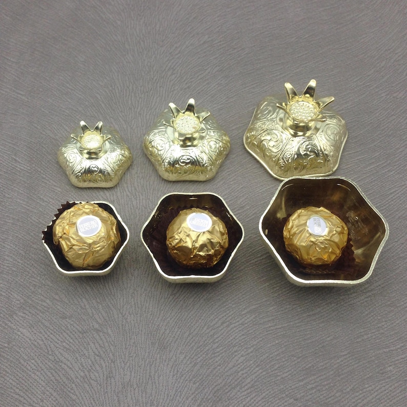May include: Six gold-colored metal containers shaped like pomegranates. The containers are in various sizes and some have a chocolate truffle inside.