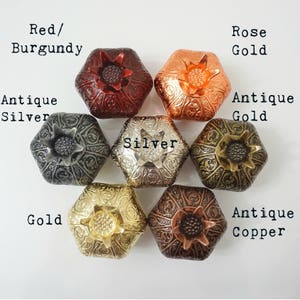 May include: Six hexagonal decorative boxes with intricate designs in various metallic finishes: red/burgundy, antique silver, silver, antique gold, gold, and antique copper. The boxes are arranged in a circle with the text "Red/Burgundy", "Antique Silver", "Silver", "Rose Gold", "Antique Gold", and "Antique Copper" written around them.