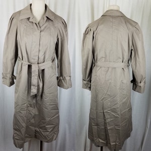 May include: A tan trench coat displayed on a mannequin. The coat features a belted waist, buttoned cuffs, and a classic collar. The coat is shown from the front and back, showcasing its full length and design details. The fabric appears to be a lightweight material.