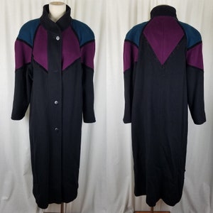 May include: A long black coat with a high collar and button closure. The coat features teal and purple color block accents on the shoulders and upper back. The coat is displayed on a mannequin.