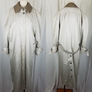 May include: A light beige trench coat with a contrasting tan collar. The coat features a button-down front, adjustable cuffs, and a belt detail at the back. The coat is displayed on a mannequin.