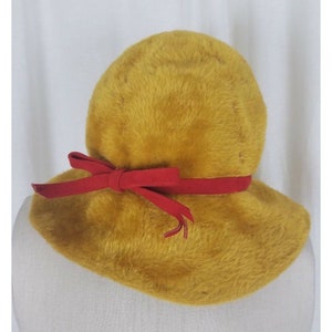 May include: A mustard yellow fuzzy hat with a wide brim and a red velvet ribbon tied in a bow.
