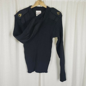 May include: Black ribbed knit sweater with a v-neck and gold shoulder patches. The sweater has long sleeves and a relaxed fit.