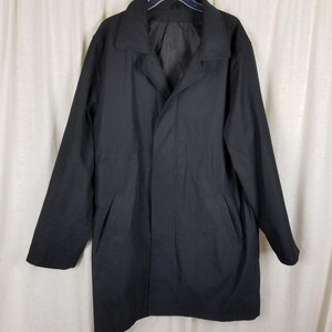 May include: A black coat with a collared neckline and two front pockets. The coat is hanging on a hanger against a white background. The coat appears to be made of a smooth, solid fabric.