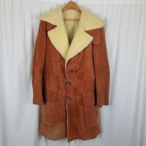 May include: A long brown suede coat with a cream coloured shearling collar and lining. The coat has a toggle closure and two large pockets.
