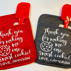 May include: Two red and gray oven mitts with a cookie and text that reads "Thank you for making me one smart cookie!"  The red mitt has the text "LOVE, ADDISON" and the gray mitt has the text "LOVE, CAMERON".