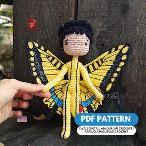 Può includere: Bambola a farfalla all'uncinetto, gialla e nera, con dettagli blu. La bambola ha capelli neri e un incarnato neutro. Il testo "PDF PATTERN" è visibile nell'immagine.
