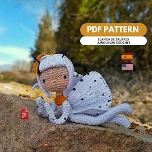 Può includere: Una bambola amigurumi all'uncinetto con capelli bianchi, viso color pesca e corpo bianco con macchie nere. La bambola ha accenti arancioni ed è sdraiata su una roccia. L'immagine include il testo "PDF PATTERN" e "BLANCA DE SALARES AMIGURUMI CROCHET."