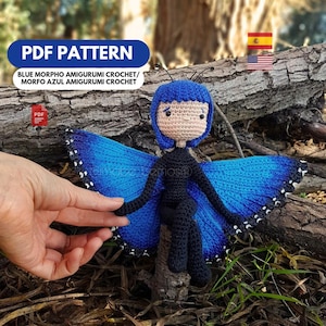 Puede incluir: Muñeca de mariposa azul tejida a ganchillo, con alas y pelo azules, cuerpo y piernas negros y cara color beige. La muñeca está sentada en un pequeño trozo de madera. El texto "PDF PATTERN" y "BLUE MORPHO AMIGURUMI CROCHET" son visibles.