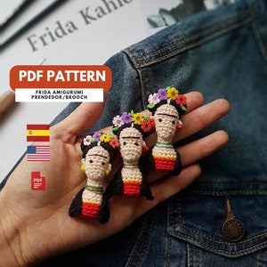 以下が含まれることがあります： 花柄のヘッドバンドをつけた、かぎ針編みで作ったフリーダ・カーロのアミグルミ人形が3体。人形は赤と黄色の服を着ており、黒い髪をしています。人形はデニムの背景に置かれています。PDF PATTERN FRIDA AMIGURUMI PRENDEDOR/BROOCH