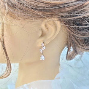 May include: Rose gold earrings with a delicate leaf design and clear cubic zirconia stones.