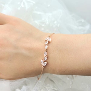 May include: A delicate gold bracelet with a chain and a design of small, clear, marquise-shaped stones set in a leaf pattern.