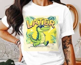 May include: White t-shirt featuring a cartoon alligator wearing sunglasses and the word "LATER" in yellow bubble letters. The alligator is green with a yellow background and palm leaves.