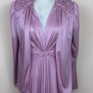 May include: A vintage lilac dress and jacket ensemble. The dress has a V-neck and a gathered waist with a decorative detail. The jacket features decorative shoulder accents and long sleeves. The outfit is displayed on a mannequin.