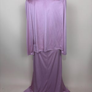 May include: A vintage lavender two-piece dress set. The set includes a long-sleeved top with shoulder pads and a floor-length skirt. The fabric has a slight sheen, and the dress is displayed on a mannequin.