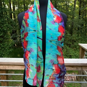 Puede incluir: Una bufanda de seda turquesa con un estampado floral abstracto colorido. La bufanda presenta tonos de rojo, rosa, morado y verde.