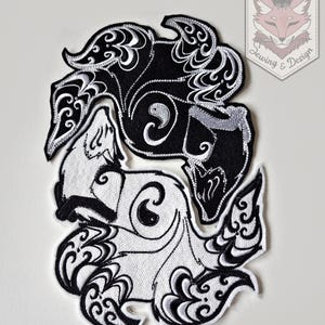 May include: Embroidered patch with a yin-yang design of two stylized foxes in black and white. The patch features detailed swirling patterns. The text "Karakitsunui Sewing & Design" is in the upper right corner.