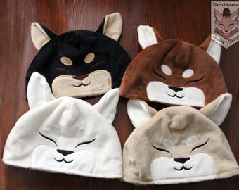 May include: Four plush animal hats, each with a different animal face. The hats are white, black, brown, and beige. The hats are all in the shape of an animal's head, with ears and a face.