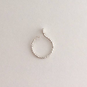 Puede incluir: Un pendiente de oreja plateado con una superficie texturizada. El pendiente tiene un diseño ondulado y abierto. Una pieza de joyería sencilla y elegante.