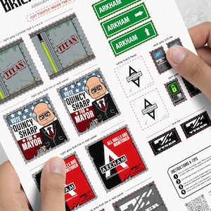 Puede incluir: Una hoja de pegatinas con diseños del universo Arkham. Incluye letreros, logotipos y gráficos con las palabras "TITAN", "ARKHAM", "TYGER" y "VOTE QUINCY SHARP FOR MAYOR". Las pegatinas son de varios colores, incluyendo verde, gris y rojo.