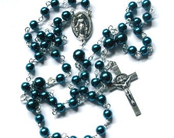 May include: Teal blue rosary beads with a silver crucifix and a silver pendant featuring an image of the Virgin Mary.