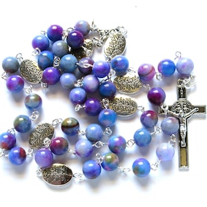 May include: A blue and purple gemstone rosary with silver beads and a silver crucifix. The beads are oval shaped and have a marbled pattern.