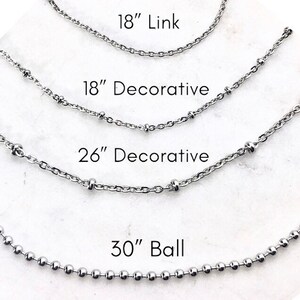May include: Four silver chains of different lengths and styles. The top chain is 18 inches long and has a simple link design. The second chain is 18 inches long and has a decorative design with small beads. The third chain is 26 inches long and has a decorative design with small beads. The bottom chain is 30 inches long and has a ball chain design.