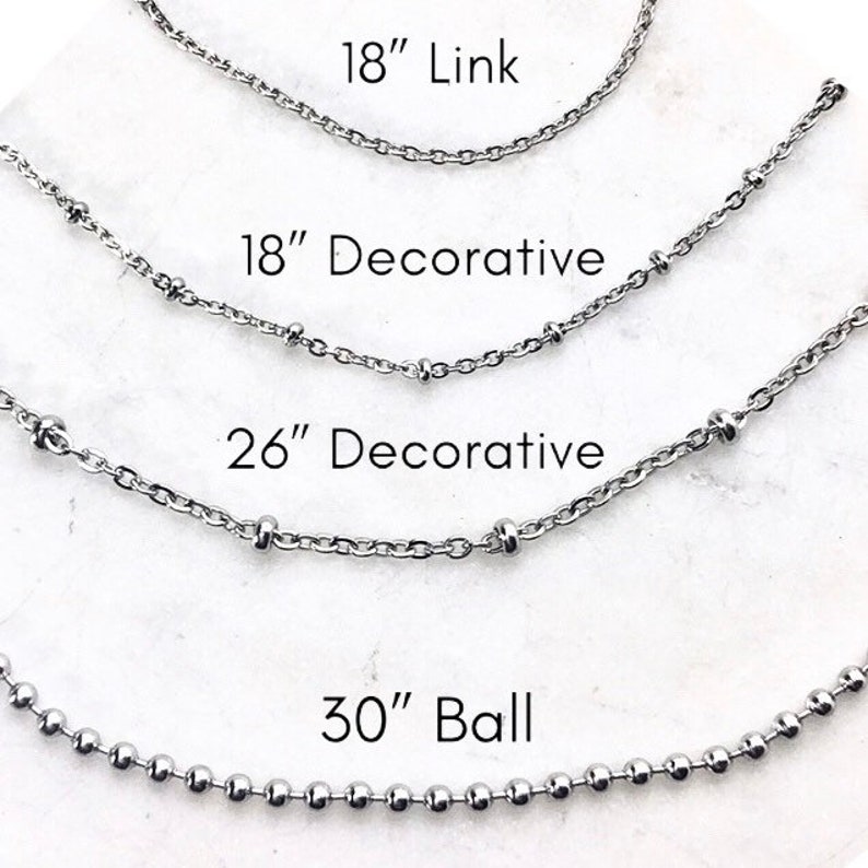 May include: Four silver chains of different lengths and styles. The top chain is 18 inches long and has a simple link design. The second chain is 18 inches long and has a decorative design with small beads. The third chain is 26 inches long and has a decorative design with small beads. The bottom chain is 30 inches long and has a ball chain design.