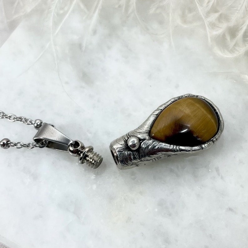 May include: A silver necklace with a pendant featuring a tiger's eye stone. The pendant is shaped like a teardrop and has a screw-on top.