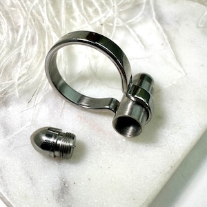 May include: A silver metal ring with a removable bullet-shaped cap. The ring is open on one side and has a smooth, rounded finish.