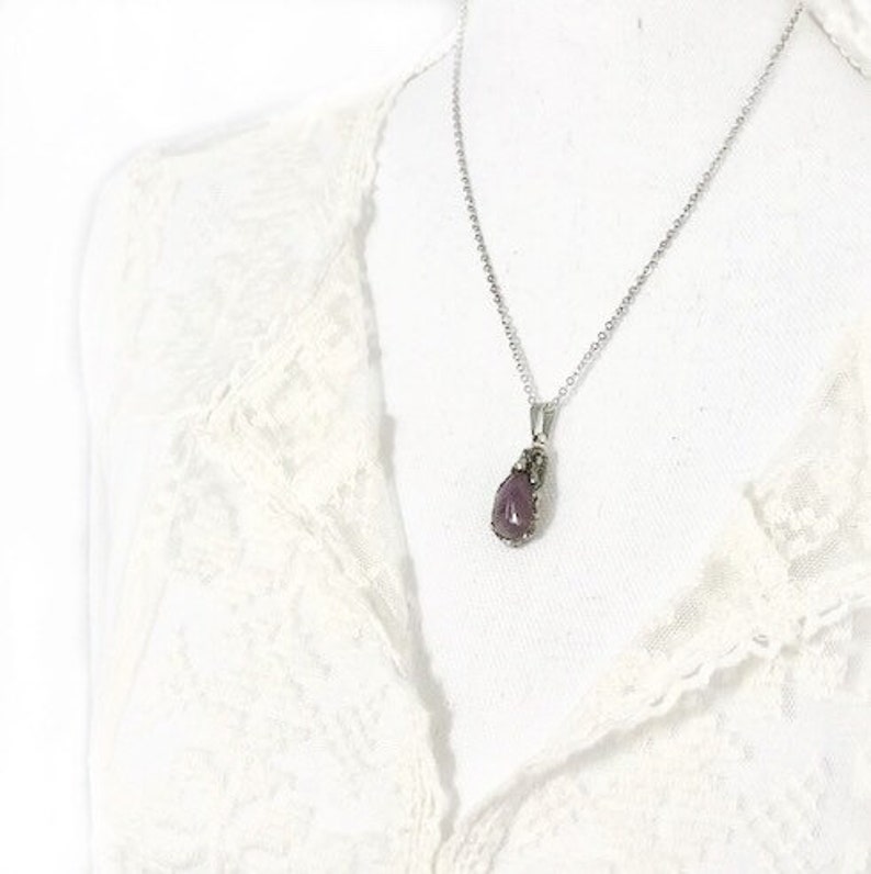 A silver chain necklace with a teardrop-shaped pendant. The pendant is a dark purple color and has a silver setting. The necklace is on a white background.