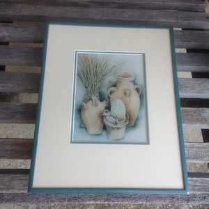 Pode incluir: Uma pintura em aquarela emoldurada de três vasos de terracota com um feixe de grama seca no fundo. Os vasos estão dispostos em uma composição de natureza morta. A pintura é emoldurada em uma moldura turquesa.