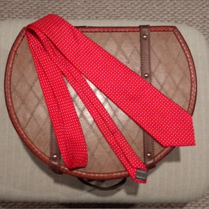 May include: A red tie with white polka dots is folded and placed on top of a brown leather suitcase.
