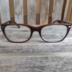 Może przedstawiać: Okulary w brązowej oprawie typu „kocie oko” z przezroczystymi szkłami.