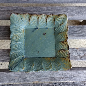 May include: A teal blue ceramic tray with a decorative, scalloped edge. The tray has a slightly distressed look, with some areas of the glaze showing signs of wear.
