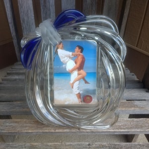 Könnte beinhalten: Ein klarer Bilderrahmen aus Glas mit einem blauen und weißen Wirbeldesign. Der Rahmen hat eine rechteckige Öffnung für ein Foto und ein blaues Banddetail. Der Rahmen steht auf einer Holzoberfläche.