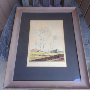 Op de afbeelding: Een ingelijst aquarel schilderij dat een landelijk landschap met een klein huis en bomen afbeeldt. Het schilderij is in een bruine houten lijst met een zwarte passe-partout.