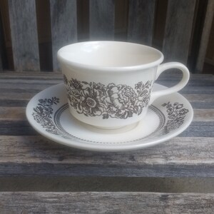 以下が含まれることがあります： 黒い花柄の白いティーカップとソーサー。カップは丸みを帯びた形をしていて、持ち手があります。ソーサーは波打った縁をしています。