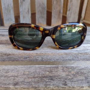 May include: Tortoiseshell sunglasses with dark lenses. The sunglasses are sitting on a wooden surface.