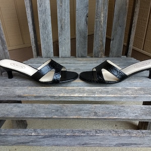 May include: A pair of black heeled sandals with a crocodile-embossed leather upper. The sandals have a low heel and a single strap across the toe.