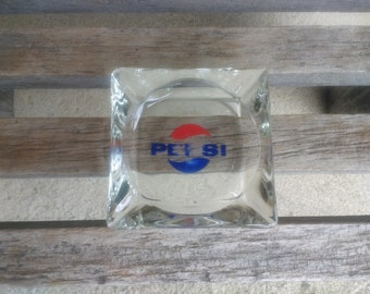 May include: A clear glass ashtray with a red and blue Pepsi logo.