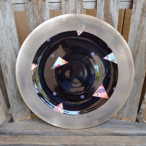 May include: A black ceramic plate with a silver rim. The plate is decorated with colourful triangles and purple polka dots.