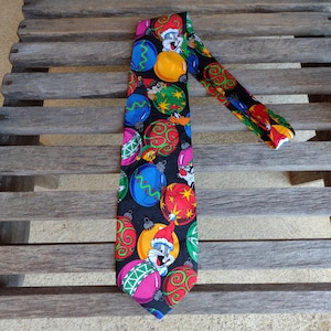 May include: A black necktie featuring colorful Christmas ornaments and cartoon characters. The tie has a repeating pattern of red, yellow, green, blue, and pink ornaments. The cartoon characters include Bugs Bunny and Daffy Duck.