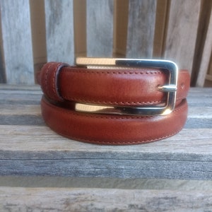 May include: A brown leather belt with a gold-toned buckle. The belt is folded in half and the buckle is closed.