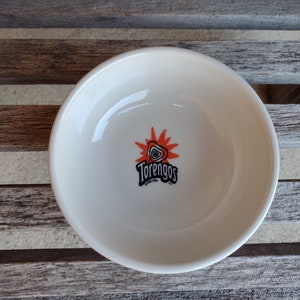 Puede incluir: Tazón de cerámica blanco con un logotipo rojo y negro que dice "Torengos" con un diseño de sol.