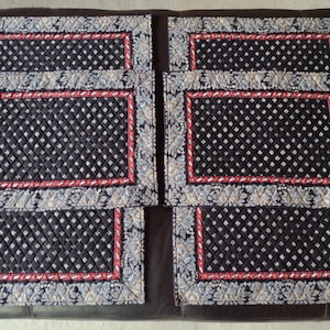 May include: Set of six black quilted placemats with a red and white floral border. The placemats have a diamond pattern.