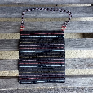 May include: A black fabric bag with a beaded strap. The bag has a striped pattern in red, blue, and gold.