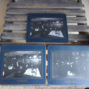 May include: Three blue and gold coasters with black and white photos of a group of people in a room. The coasters have text that reads "The Old Elizabethan Cheese The Williamson Room" and "The Old Elizabethan Cheese assembled here for Trading 1914".