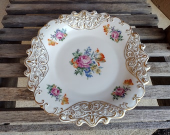 Puede incluir: Un plato de servir de porcelana blanca con un borde dorado y diseños florales. El plato tiene un borde festoneado y detalles dorados intrincados.