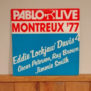 May include: A red and white vinyl record album cover with the text "PABLO LIVE MONTREUX '77" in white. The album features Eddie 'Lockjaw' Davis 4, Oscar Peterson, Ray Brown, and Jimmie Smith.